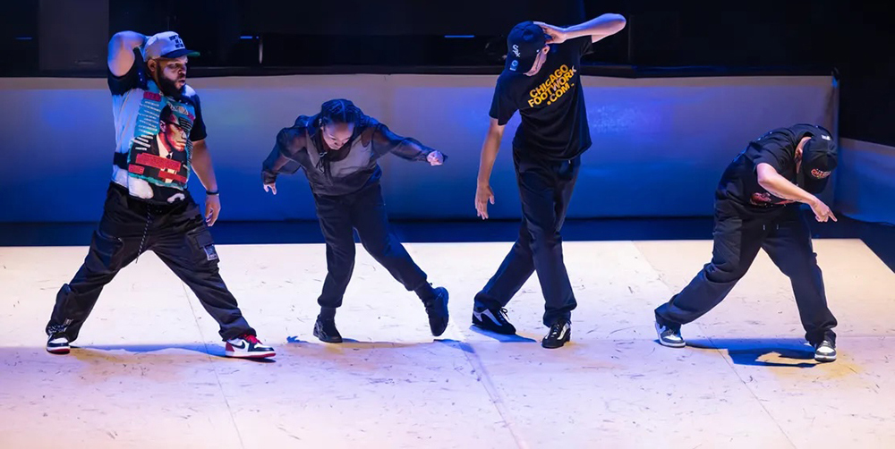 4 hip hop dancers in black baggy pants and sneakers, all in a row in different poses.