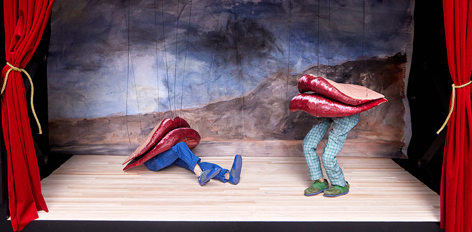 Close-up of a small black puppet theater, with red curtains, and two large puppet lips frowning, with legs.