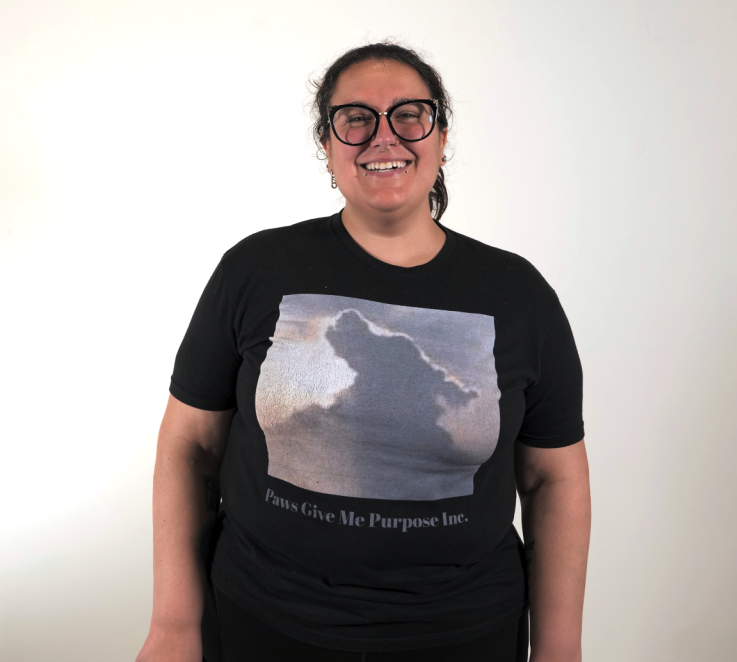 Alexis wearing a black t-shirt and glasses standing and smiling at the camera