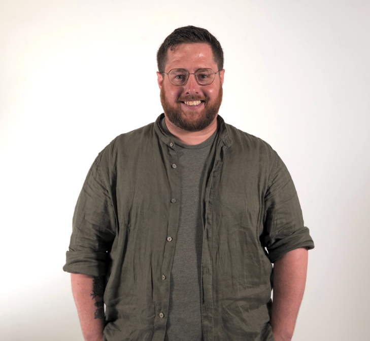 Chris Devery wearing a green shirt and glasses, smiling at the camera.