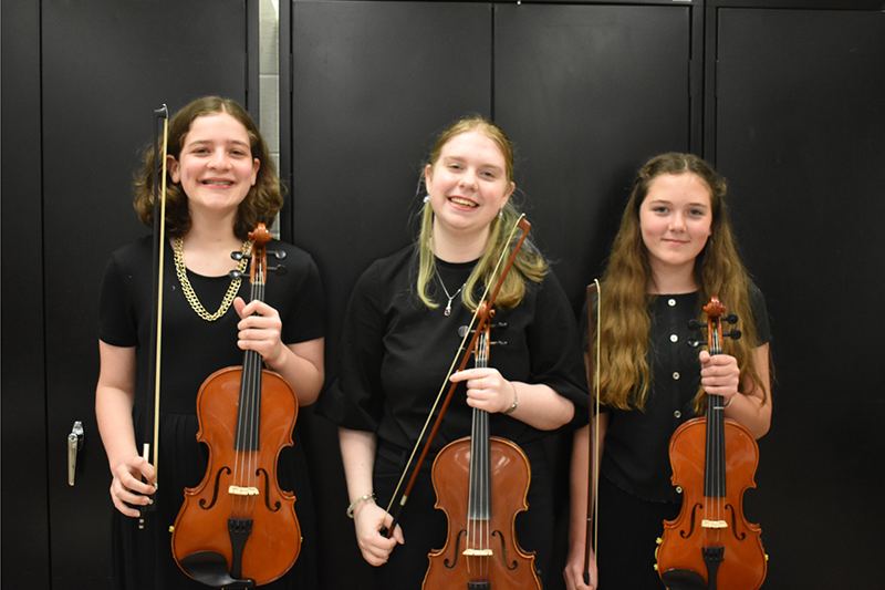 3 female students in concert black holding their violins