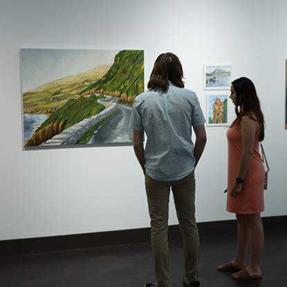 Visitors look at a painting hanging on a white wall.