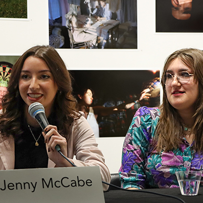 Two speakers are sitting at a table with microphones.