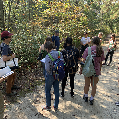 A group gathers on a dirt path in a wooded area.