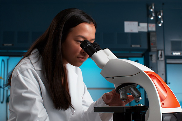 A close up of a student looking through a microscope.