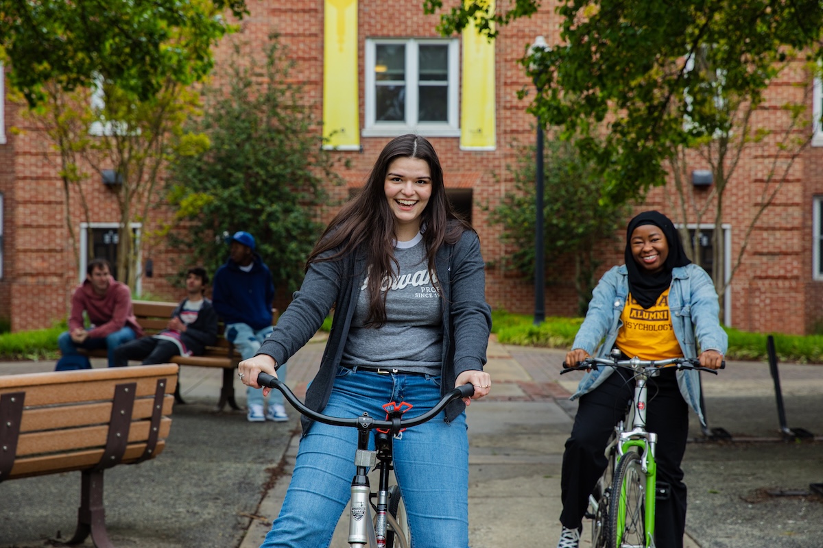 Two students on bicycles smiling at the camera.