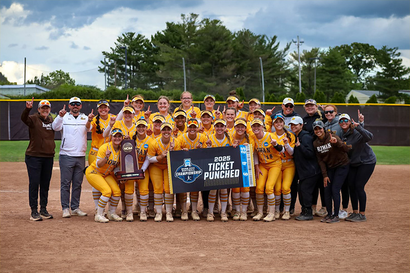 The 2025 softball team stand with a post highlighting their season win.