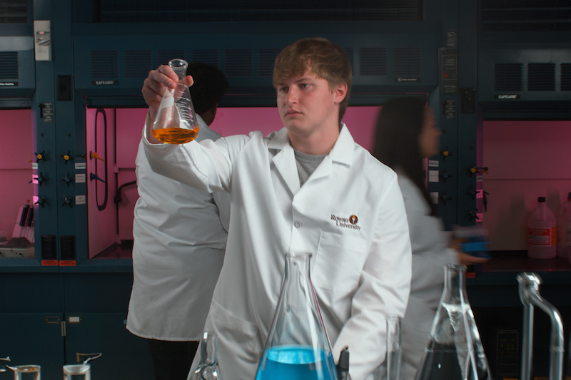 A close up image of a science major holding a beaker toward the camera.