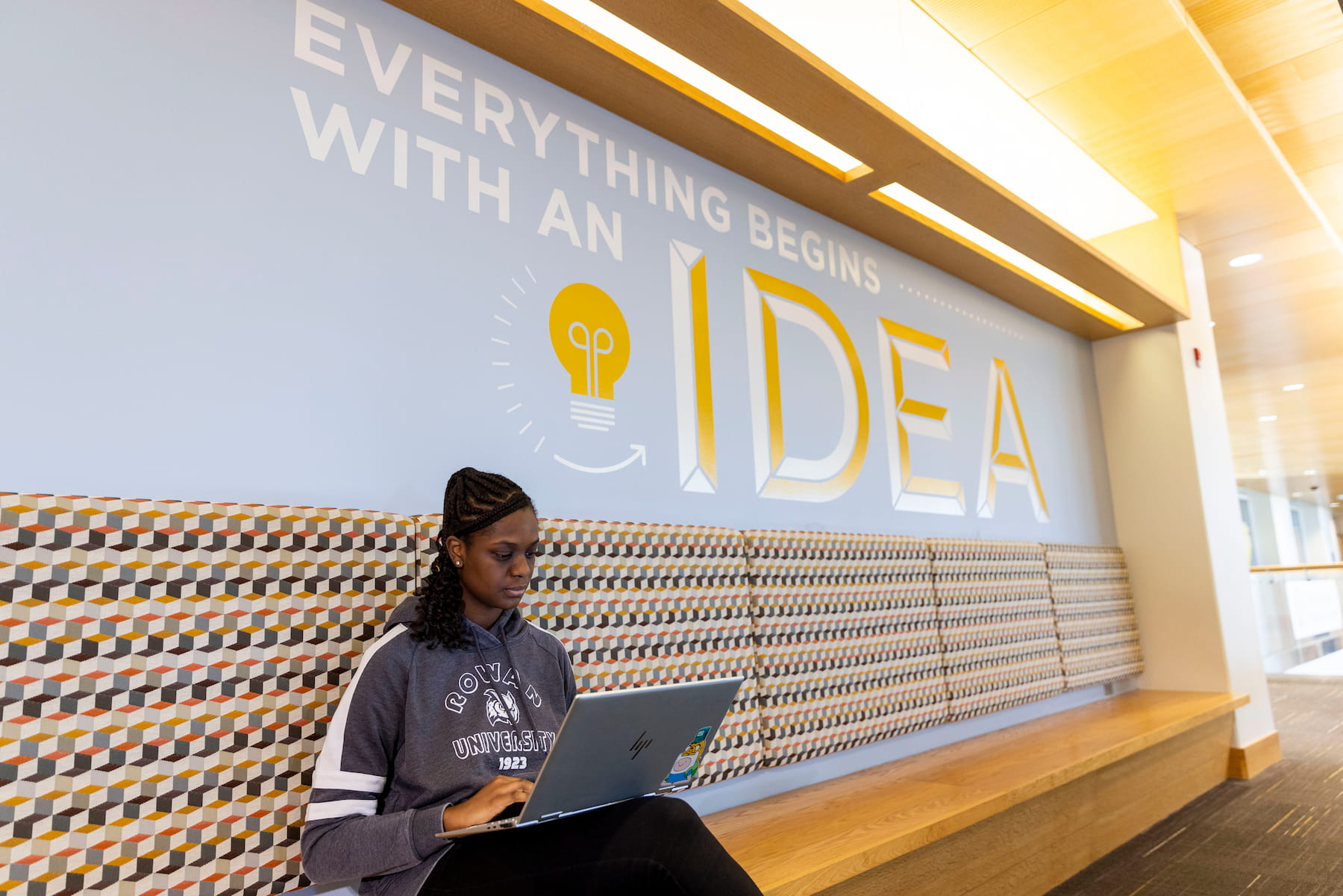 Student working on a laptop in front of a wall decal stating 'Everything begins with an idea with a light bulb' image