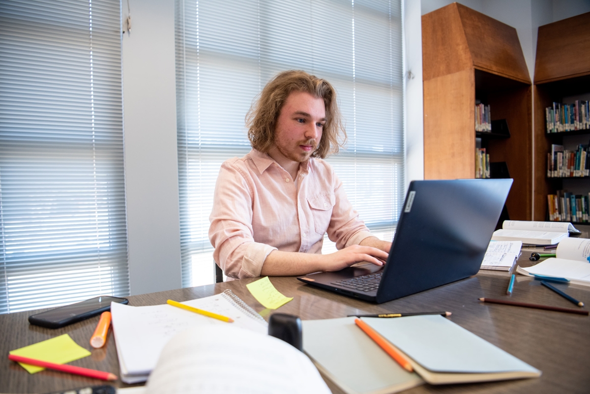 A student works on their laptop at a desk. 