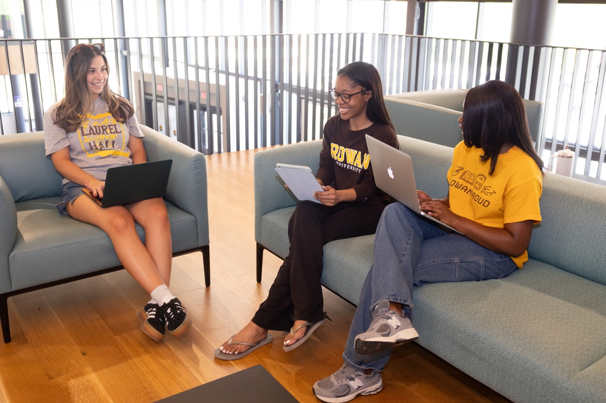 Three students chatting while working on their laptops.