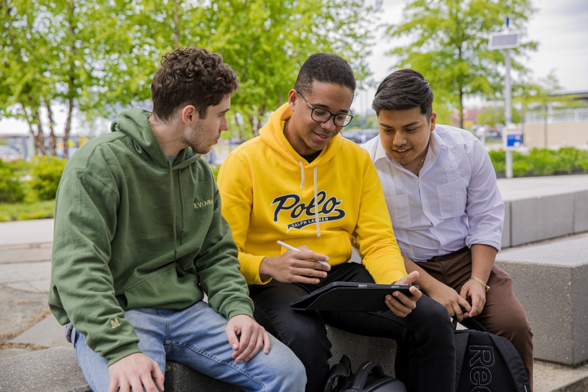 Three students sit together and look at a tablet.