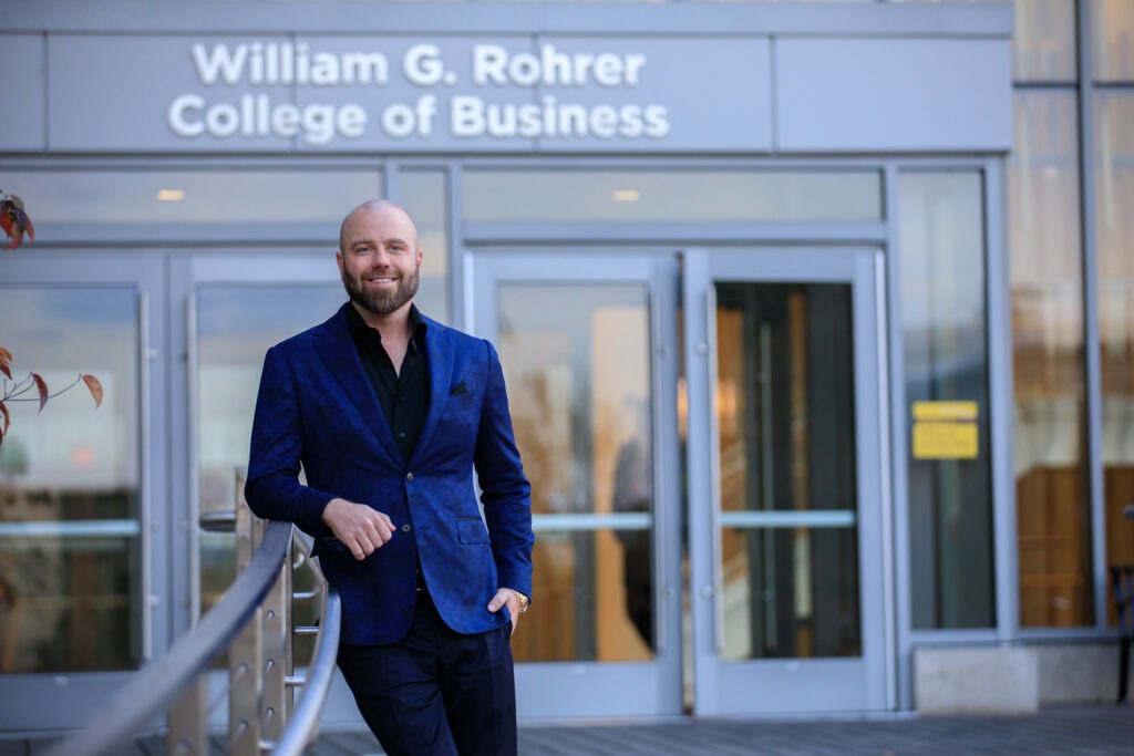 A student stands while smiling in front of Business Hall on Rowan University's main campus in Glassboro, NJ. 