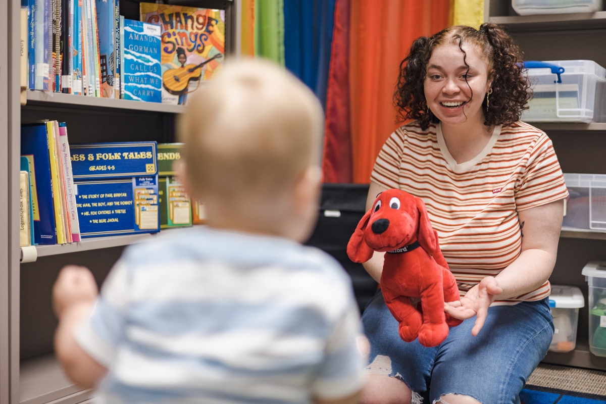 A Rowan student holds a toy while smiling at a child.