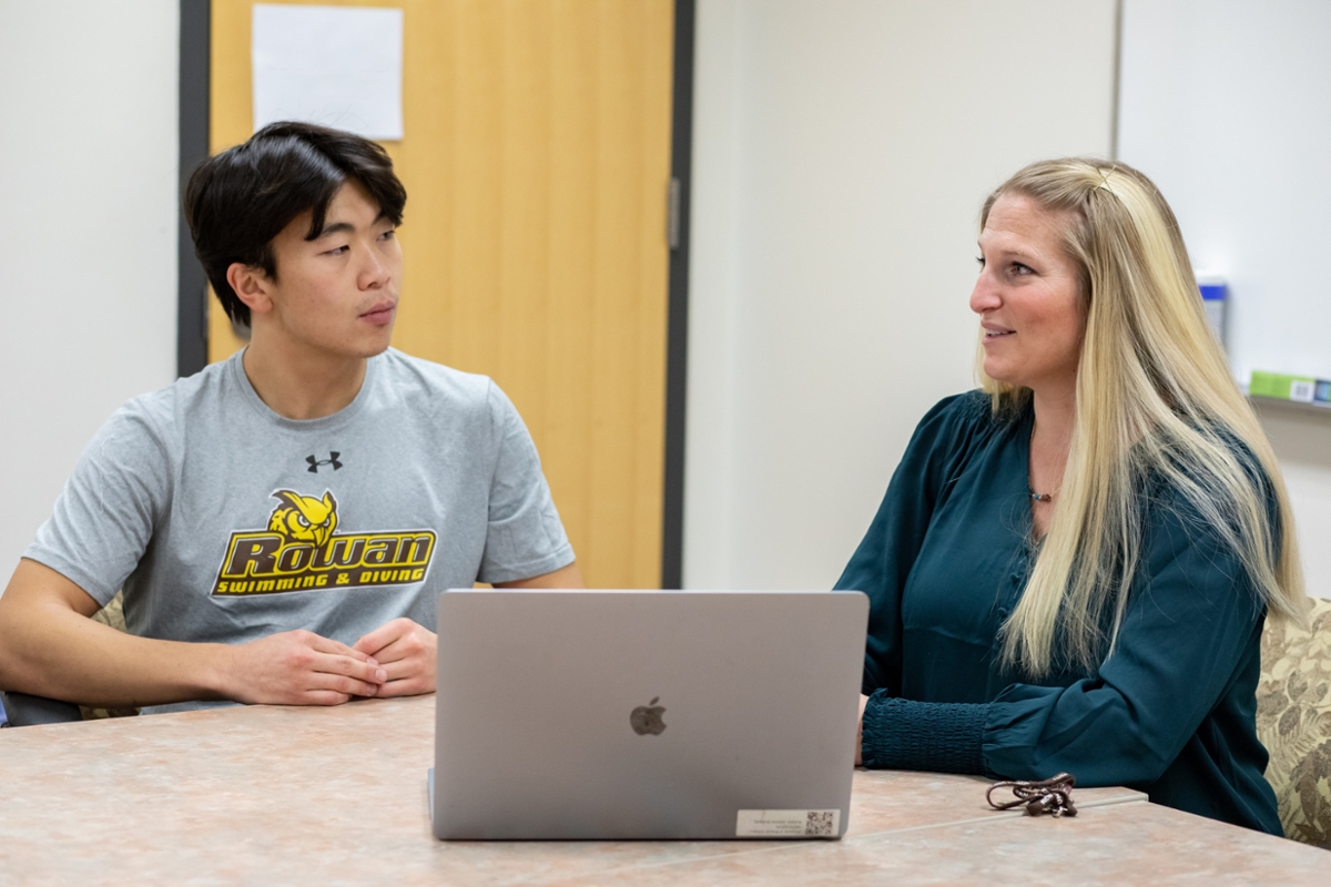 A Rowan student sits and talks with a staff member in front of a laptop.