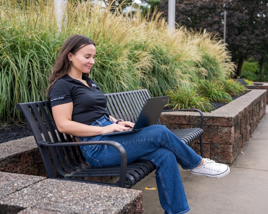 A student sits on a bench with their computer on Rowan's main campus in Glassboro, NJ.