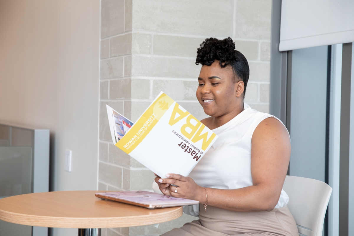 A Rowan student sits at a table while reading through information pertaining to the MBA program.