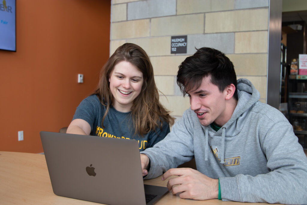 Two students work together while looking at a computer.
