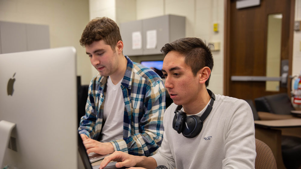 Two Rowan students work on desktop computers.