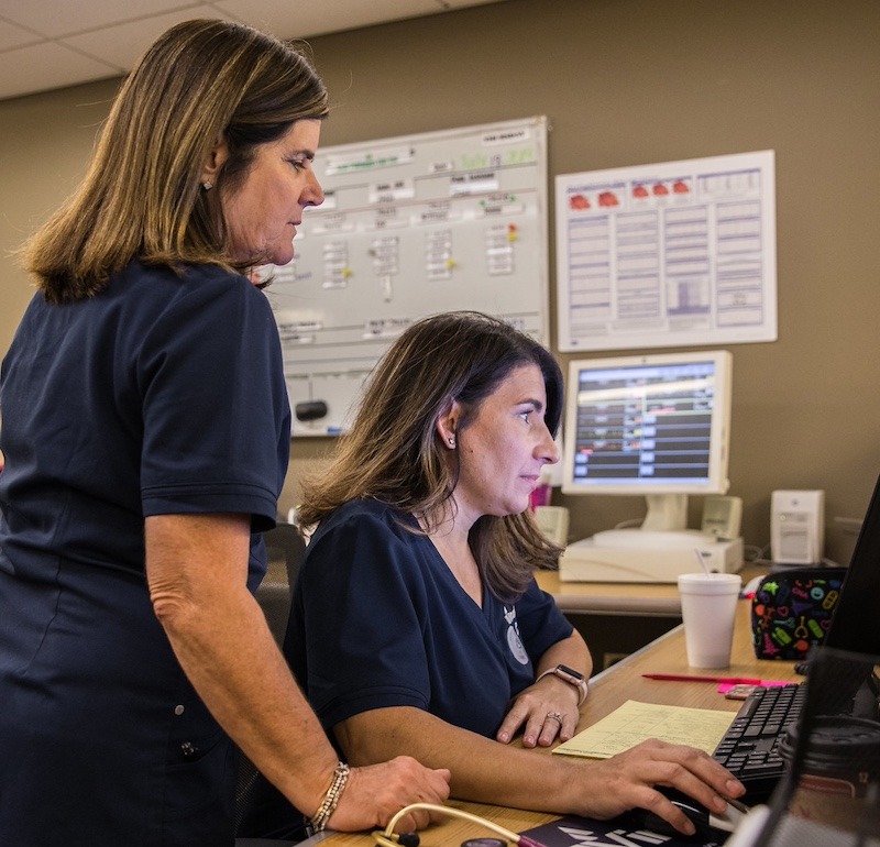 Two nurses work together while looking at a computer screen.