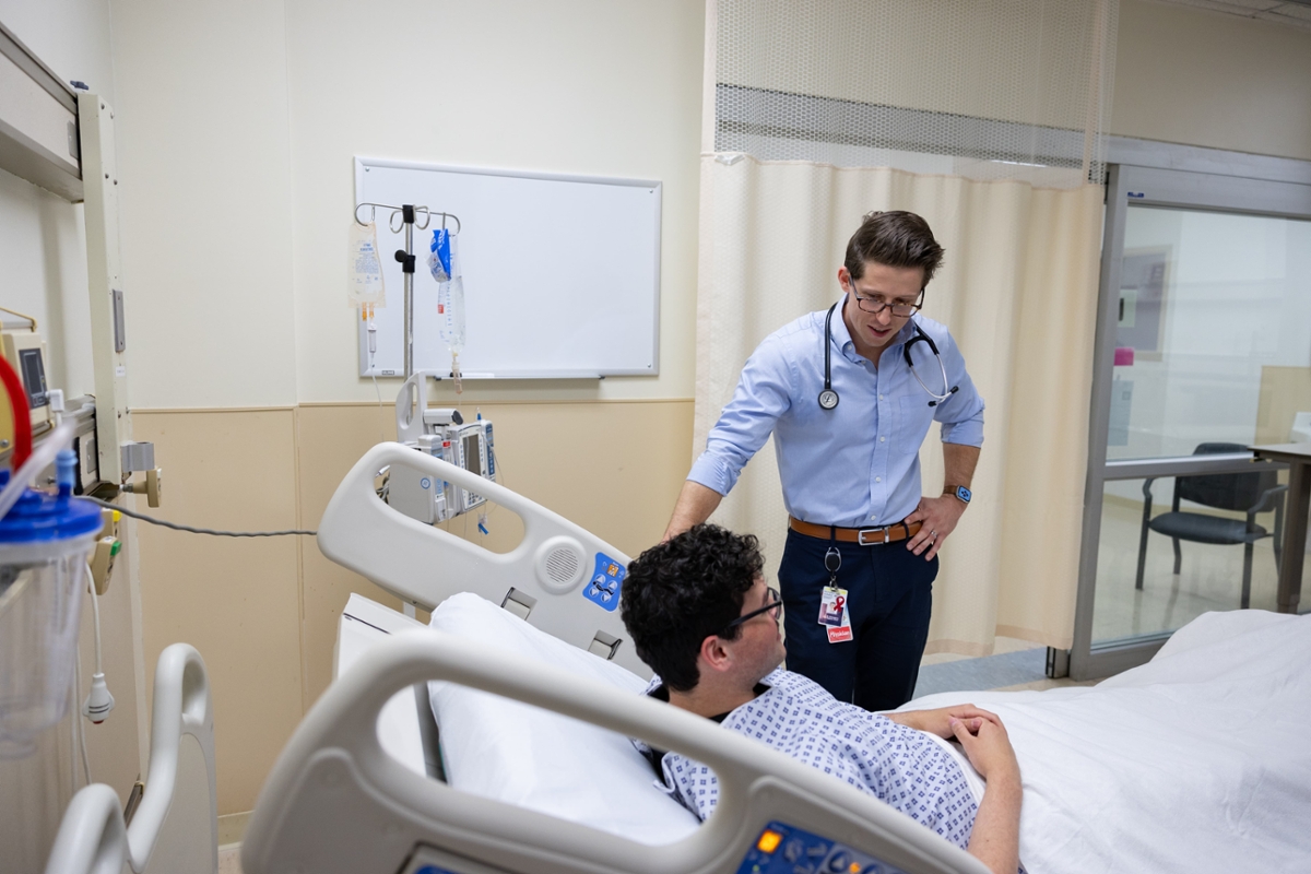 A medical student talks with a patient at bedside.