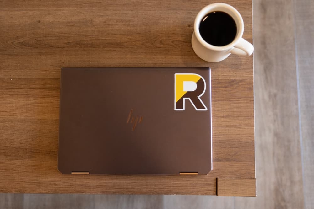 An aerial view of a laptop with a Rowan sticker sitting on a desk next to a coffee mug.