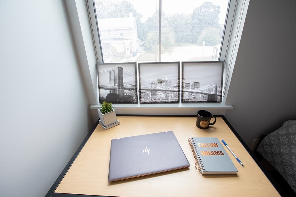 A laptop and a journal sitting on a desk before a window.