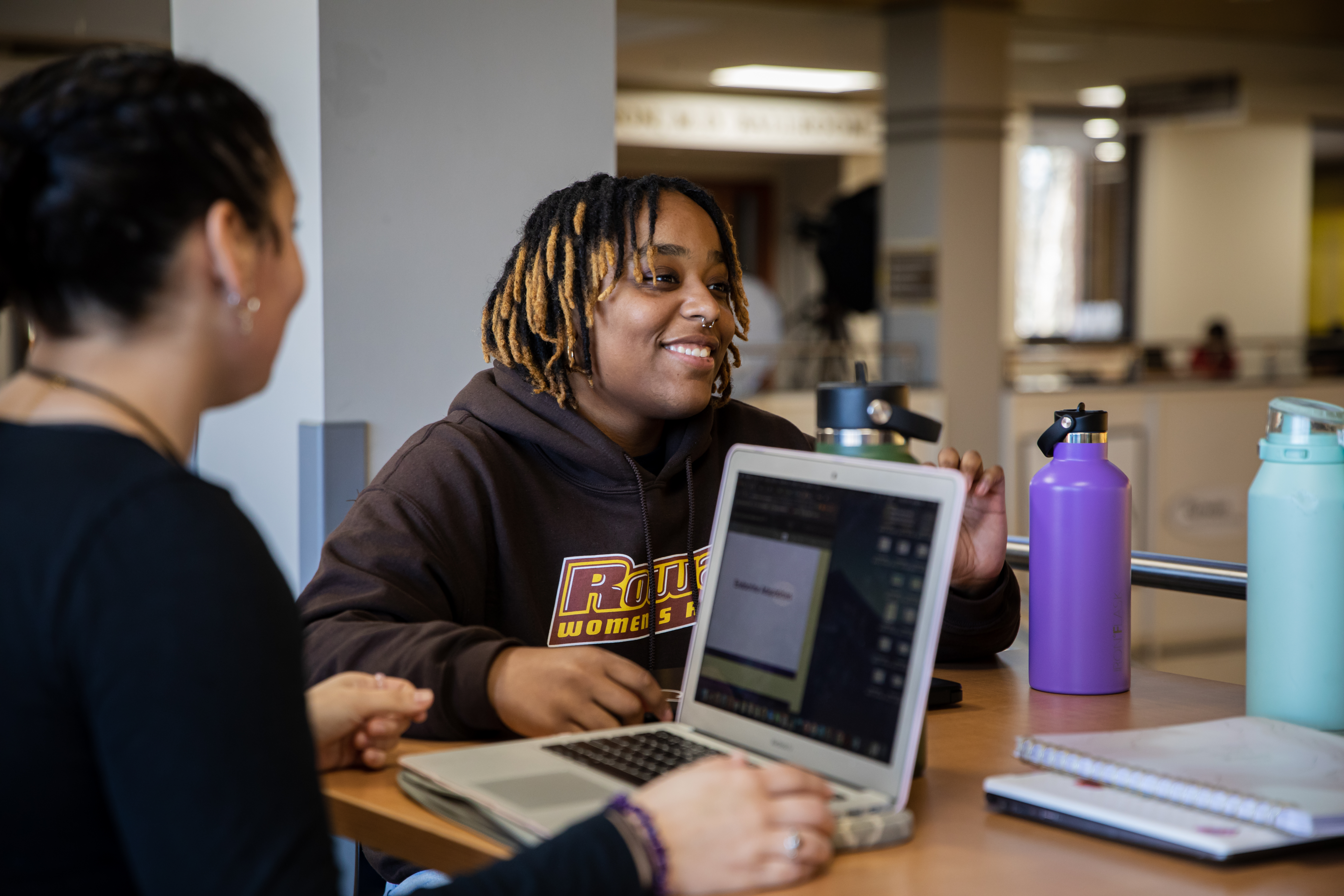 A student smiles while at the library talking with their peers.