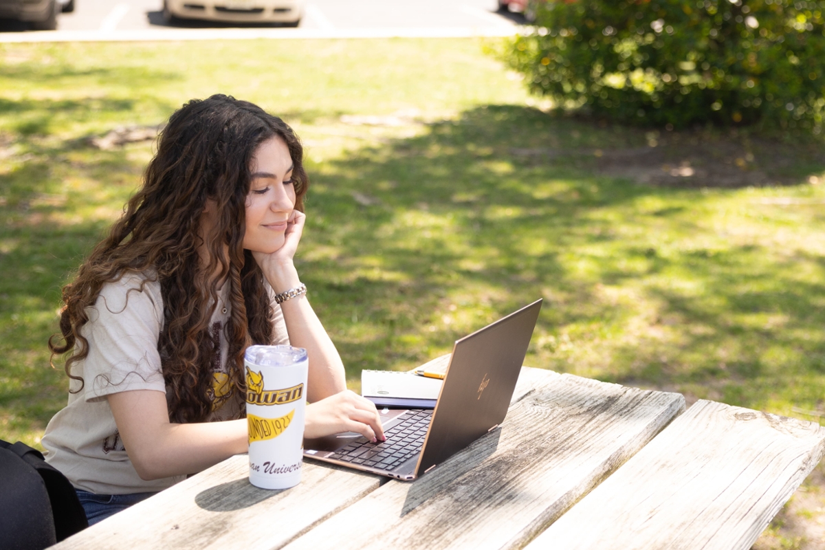 A Rowan student sits and works on their laptop at a picnic table.