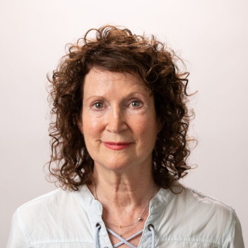 Cynthia Haveson Veloric with dark curly hair wearing a light blue shirt smiling at the camera.