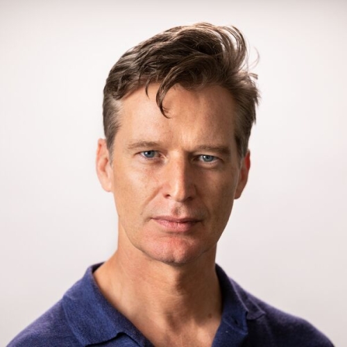 Eugene Hughes wearing a blue collared shirt and short hair, smiling at the camera.