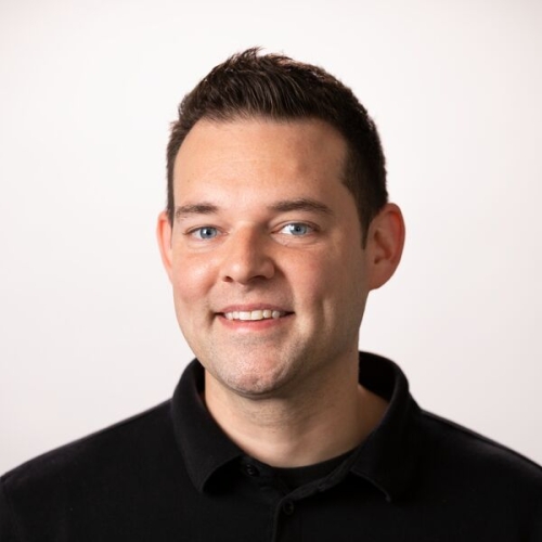 Frank Machos wearing a black collared shirt with short dark hair smiling at the camera.