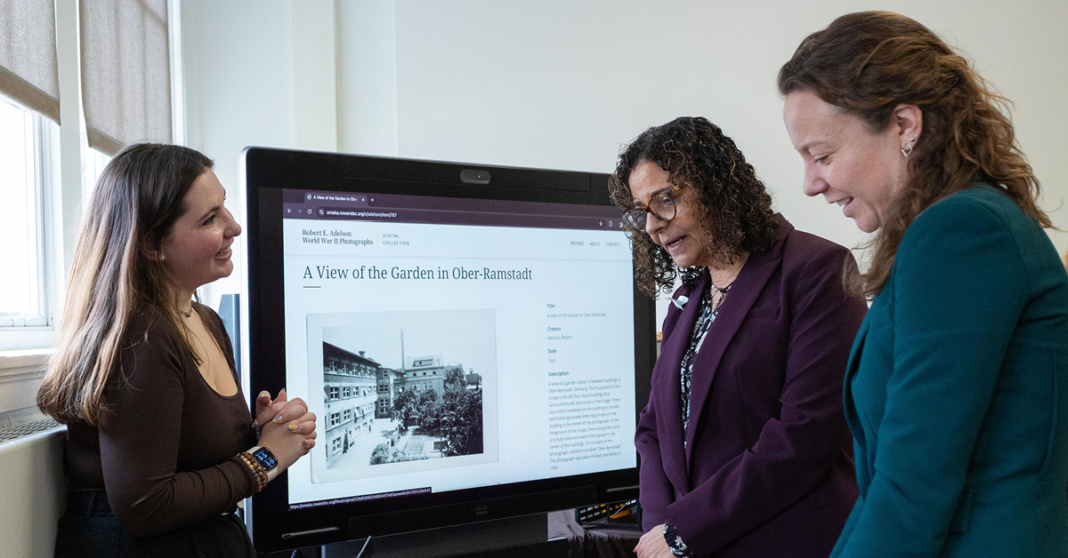 A student presents a digital project on a monitor to administrators and faculty