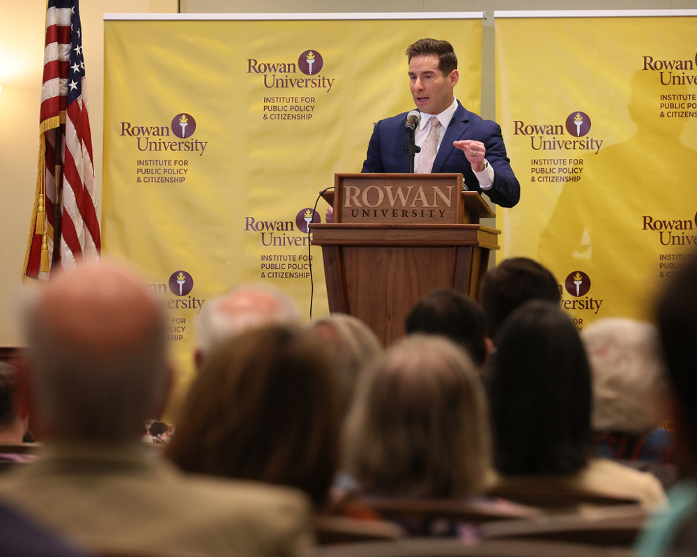 Elie Honig, CNN Senior Legal Analyst, standing at a podium in a suit with RIPPAC banners in the background