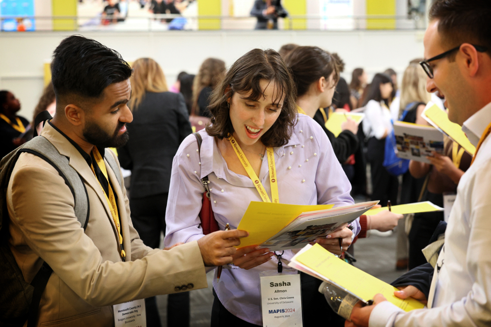 Two male students and one female students compare bingo sheets during the MAPIS2024 networking activity