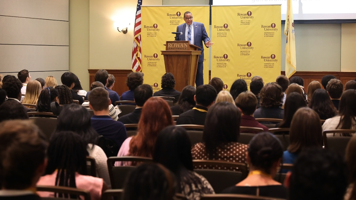 New Jersey Lieutenant Governor Dale Caldwell standing on a stage in behind a podium, speaking to a room of college students