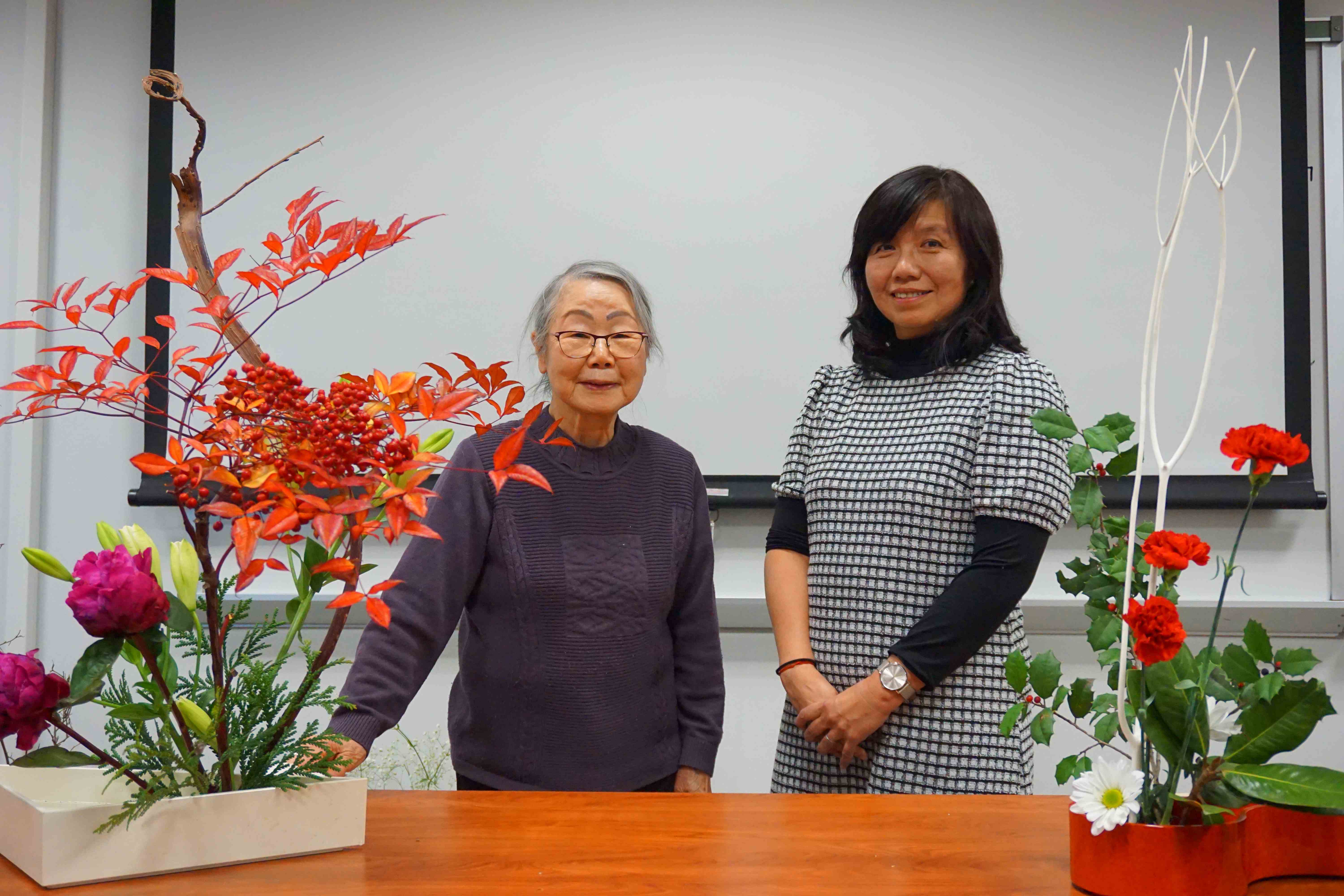 Professor Matsumura Dusk and Mrs. Mariko Ono smiling behind an Ikebana demonstration.
