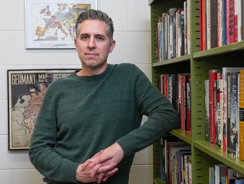 Portrait of Rowan researcher and historian Mikkel Dack standing in front of a bookcase