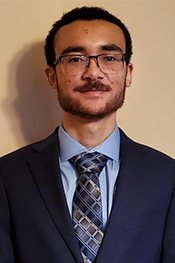 Isiah Hiatt smiles while wearing a navy blue suit, blue button down shirt and a blue patterned tie