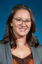Nicole Hinds smile in a headshot while wearing glasses, a grey blazer and red shirt