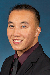 Quy Nguyen smiles into the camera while wearing a grey suit jacket, tie, and burgundy shirt