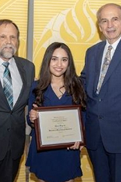 Delis Tejeda smiles while holding a certificate between two men