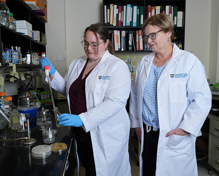 a researcher works with a student standing at a lab table